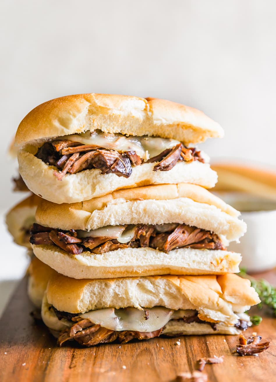 French Dip Sandwich, or French Dip Au Jus, is a delicious and easy way to enjoy crockpot beef! We create a Beef Au Jus sandwich with tender beef, provolone cheese, toasty bread, and of course the dipping sauce. Such a simple crockpot french dip recipe that the entire family will love. This French Dip Sandwich Recipe is a winner! stacked crock pot french dip sandwiches