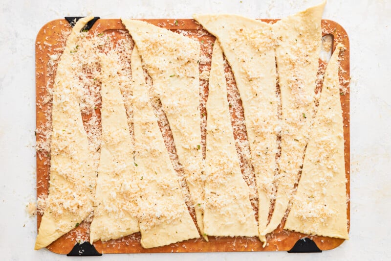 crescent rolls coated in cheese and seasoning salt on a wooden cutting board.