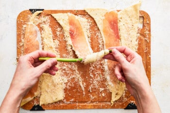a hand rolling an asparagus spear in crescent dough lined with prosciutto.