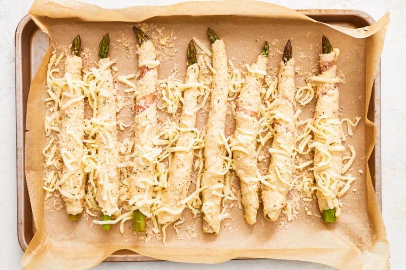 8 unbaked asparagus crescent rolls topped with cheese on a lined baking sheet.