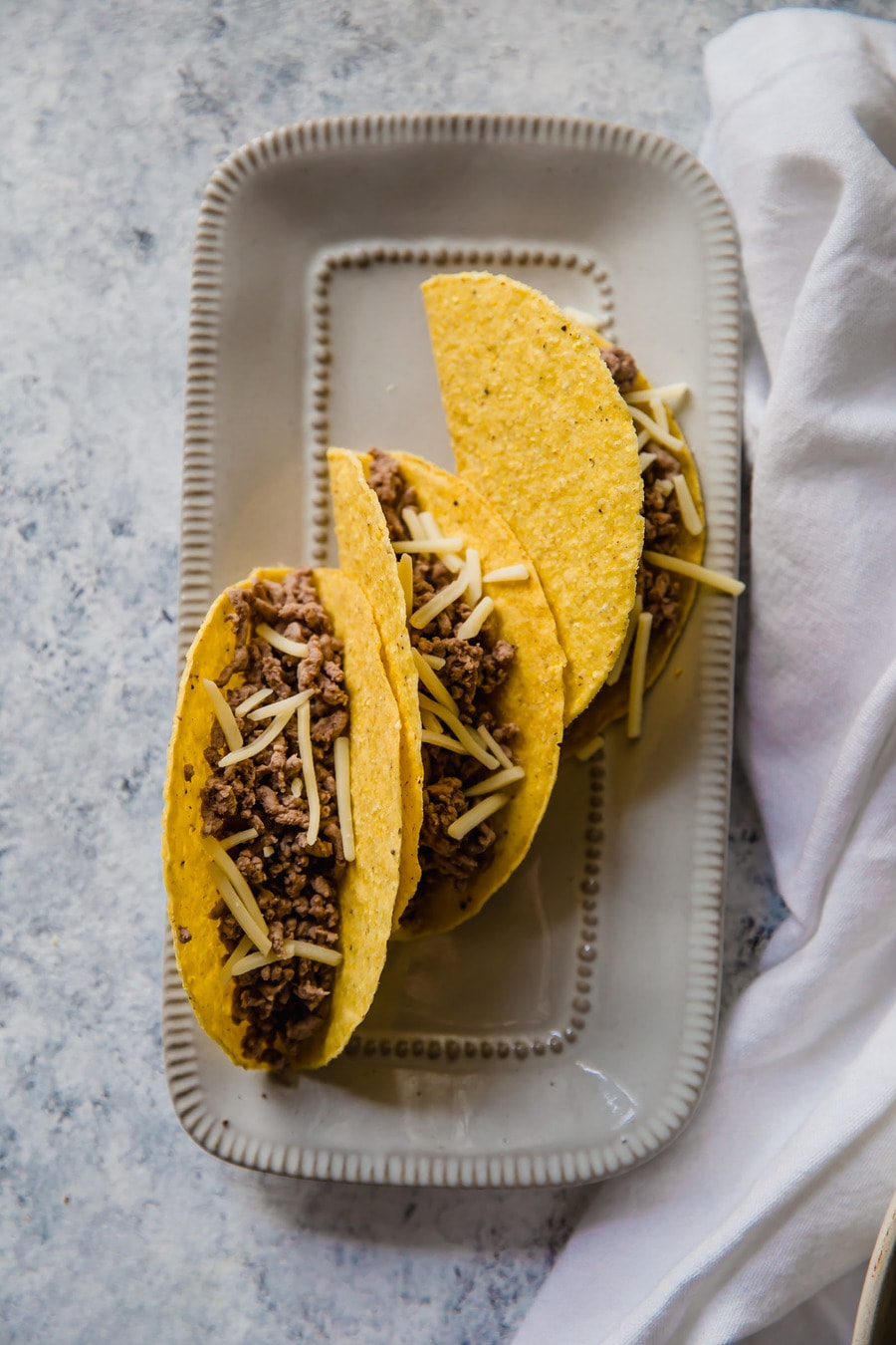 three taco shells filled with ground beef, on a white serving platter
