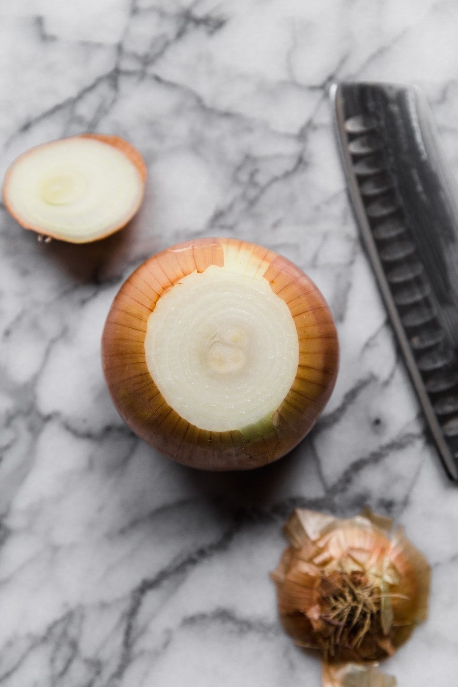 an onion on a marble surface, next to a knife