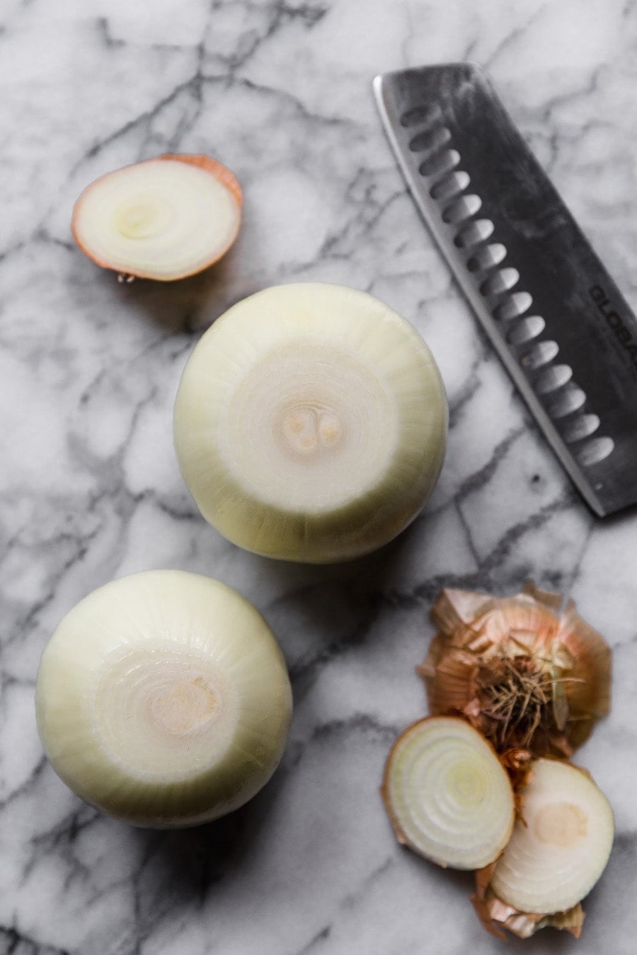how to cut an onion: peeled onion on a marble surface, next to a knife