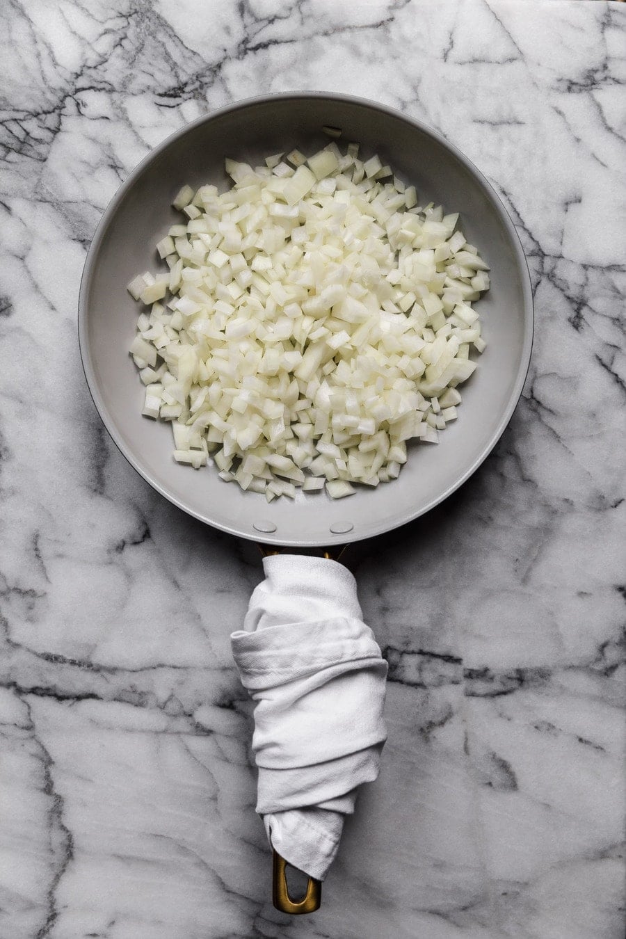 diced onion in a skillet on a marble surface