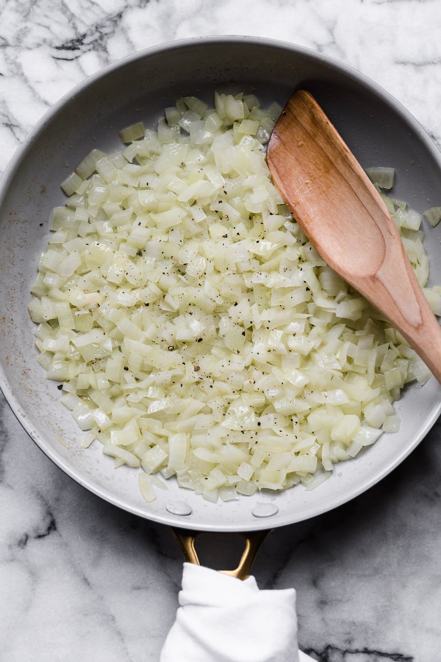 how to saute onions: minced onion in a skillet with a wooden spoon