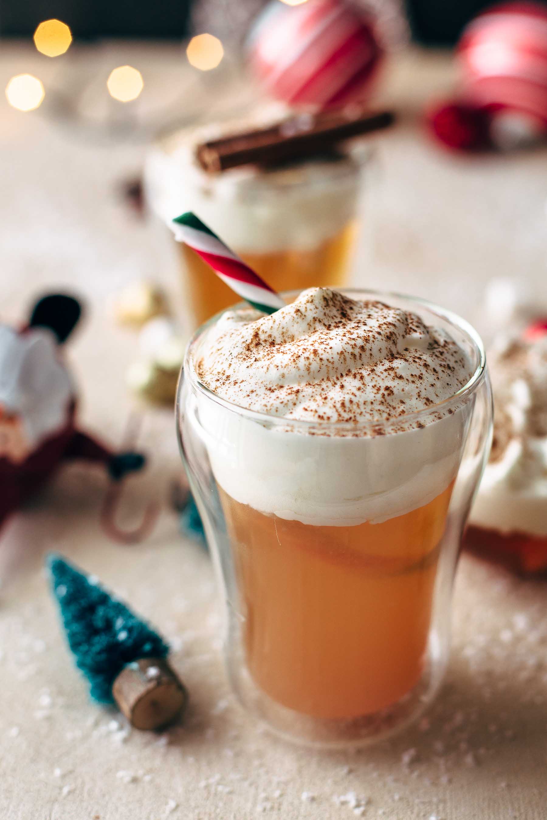 A glass of caramel apple hot toddy surrounded by christmas ornaments