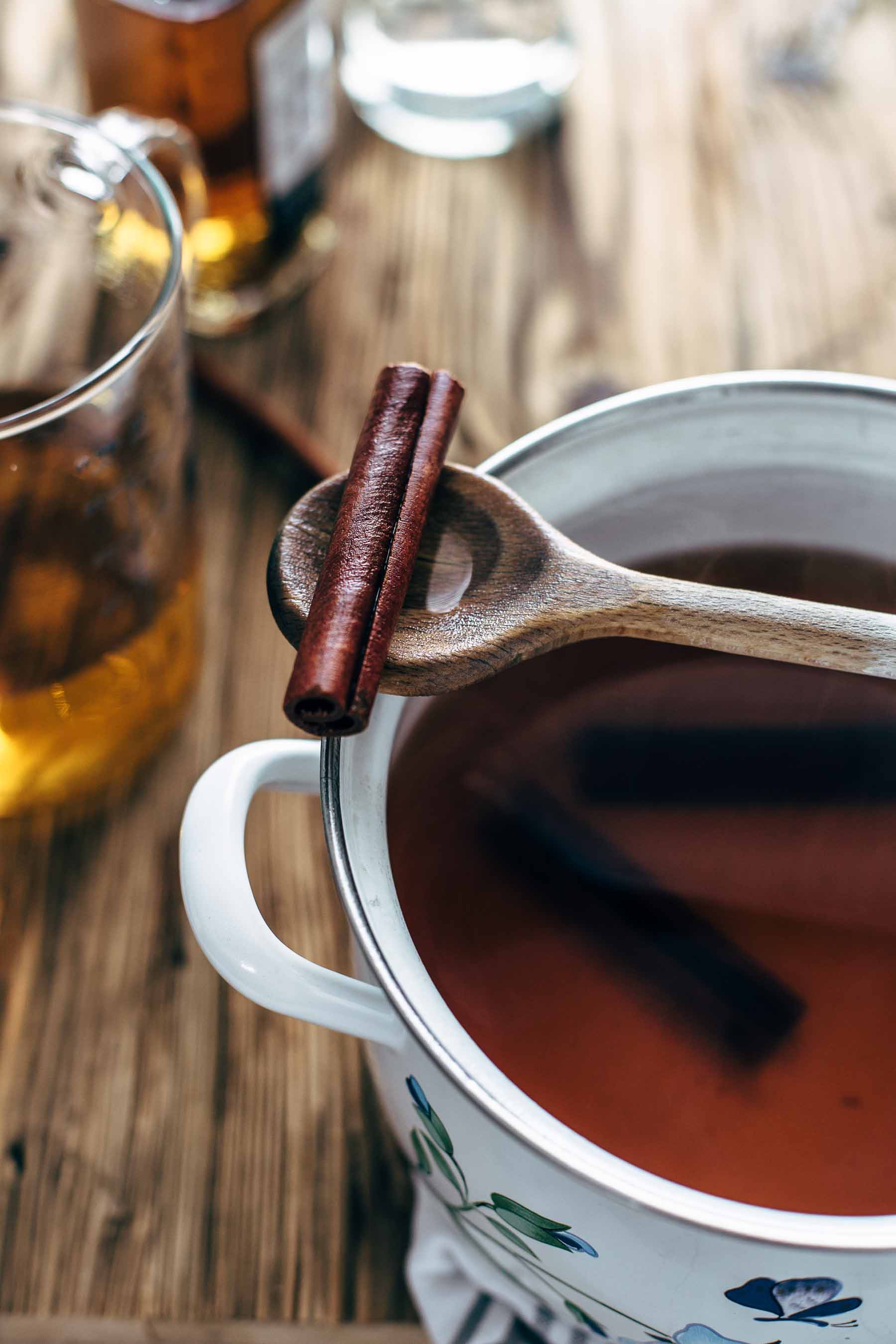 A wooden spoon with a cinnamon stick, sitting on top of a pot of hot toddy beverage