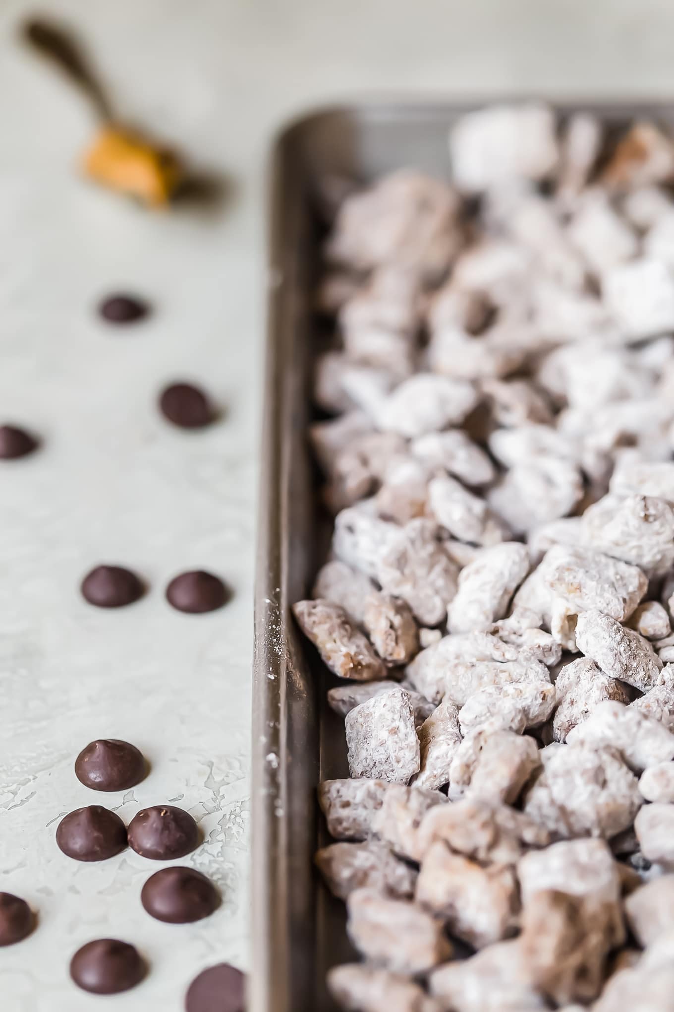 puppy chow on a baking tray with some chocolate chips next to the tray
