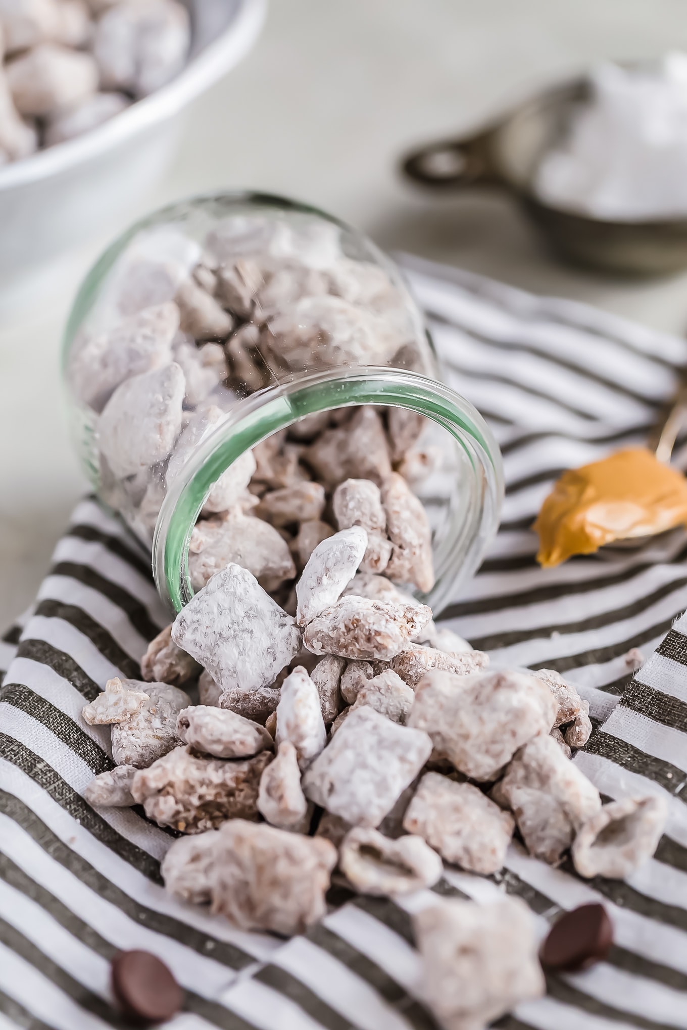 puppy chow spilling out of a glass jar onto a striped dish towel