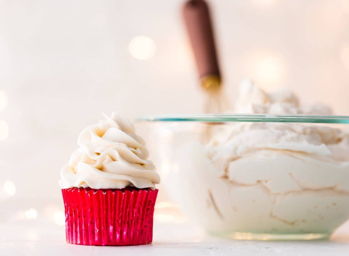 An iced cupcake next to a bowl of the frosting.