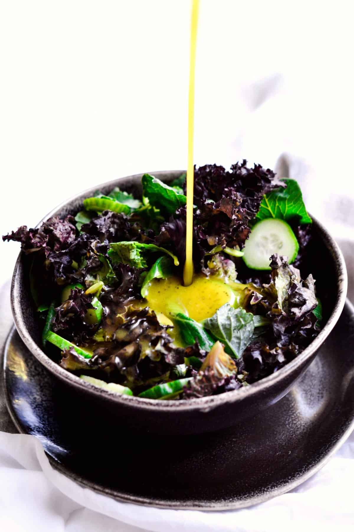 Pouring homemade Sweet and Sour Dressing over a bowl of greens