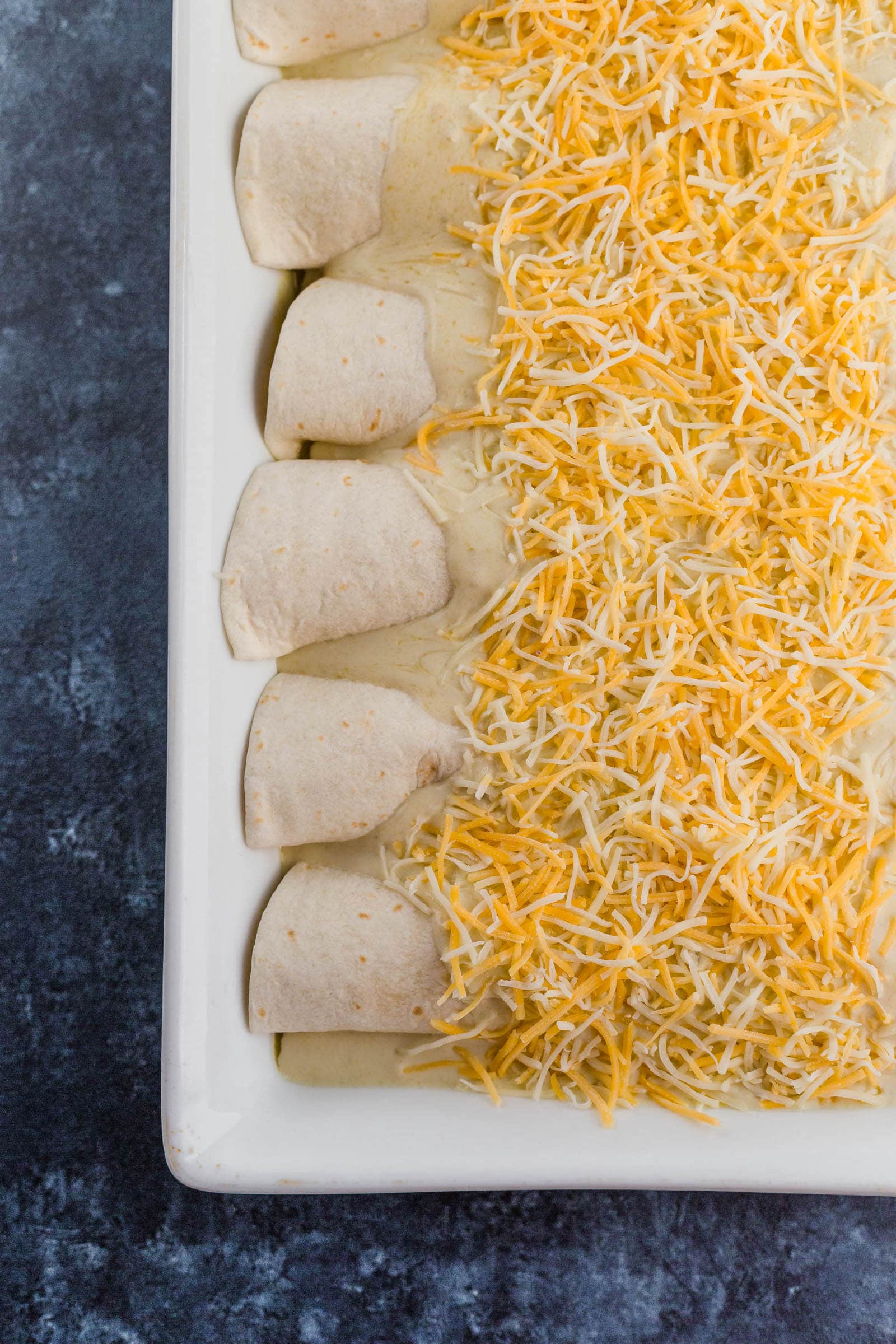 A dish of enchiladas topped with shredded cheese, before baking