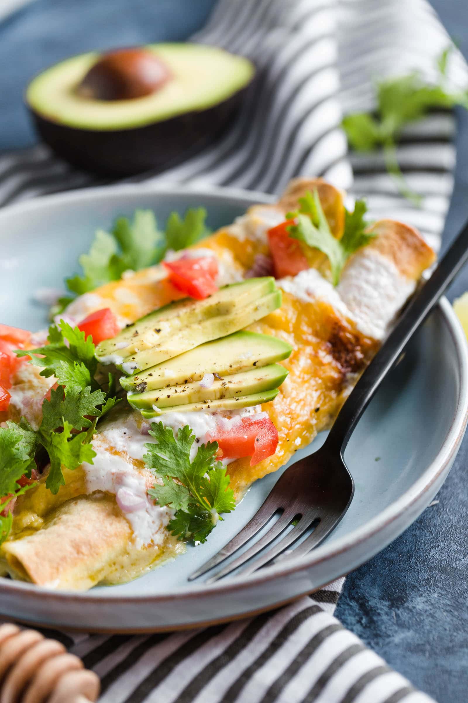 A plate of chicken enchiladas topped with avocado, cheese, and tomatoes