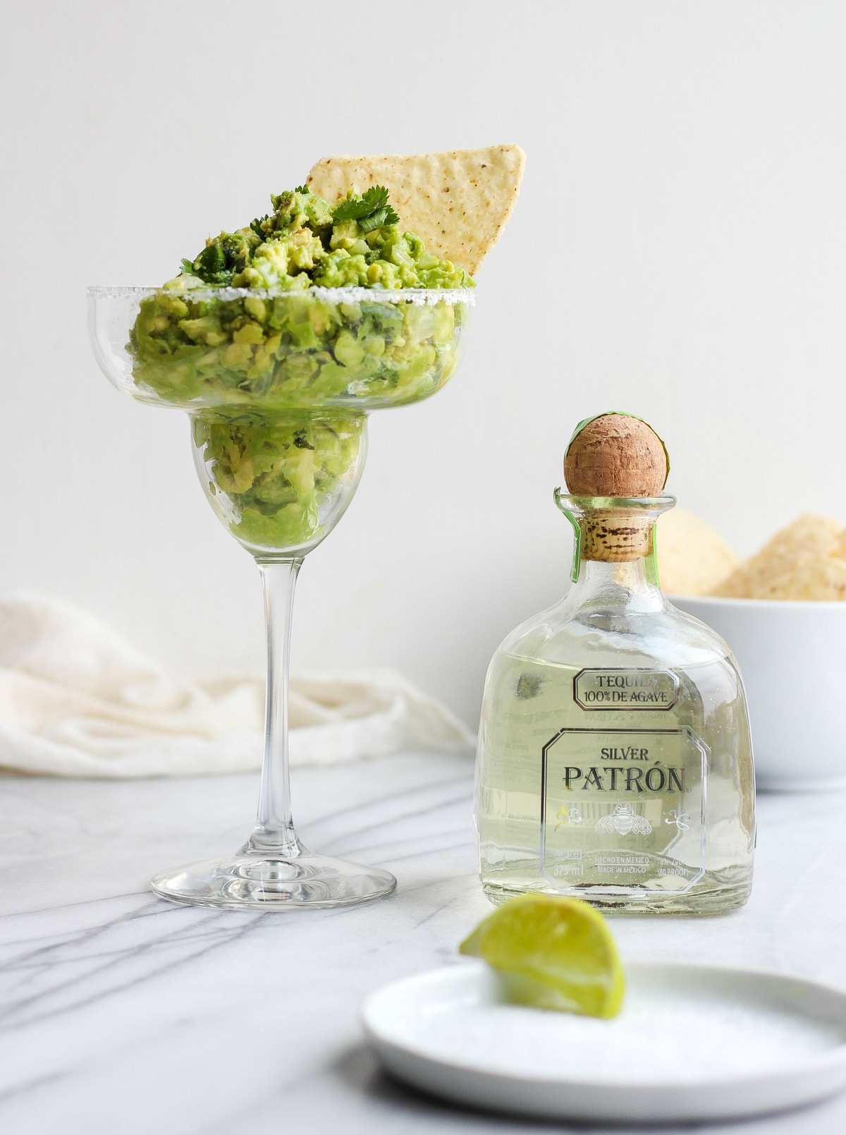 guacamole dip in a margarita glass, next to a bottle of tequila