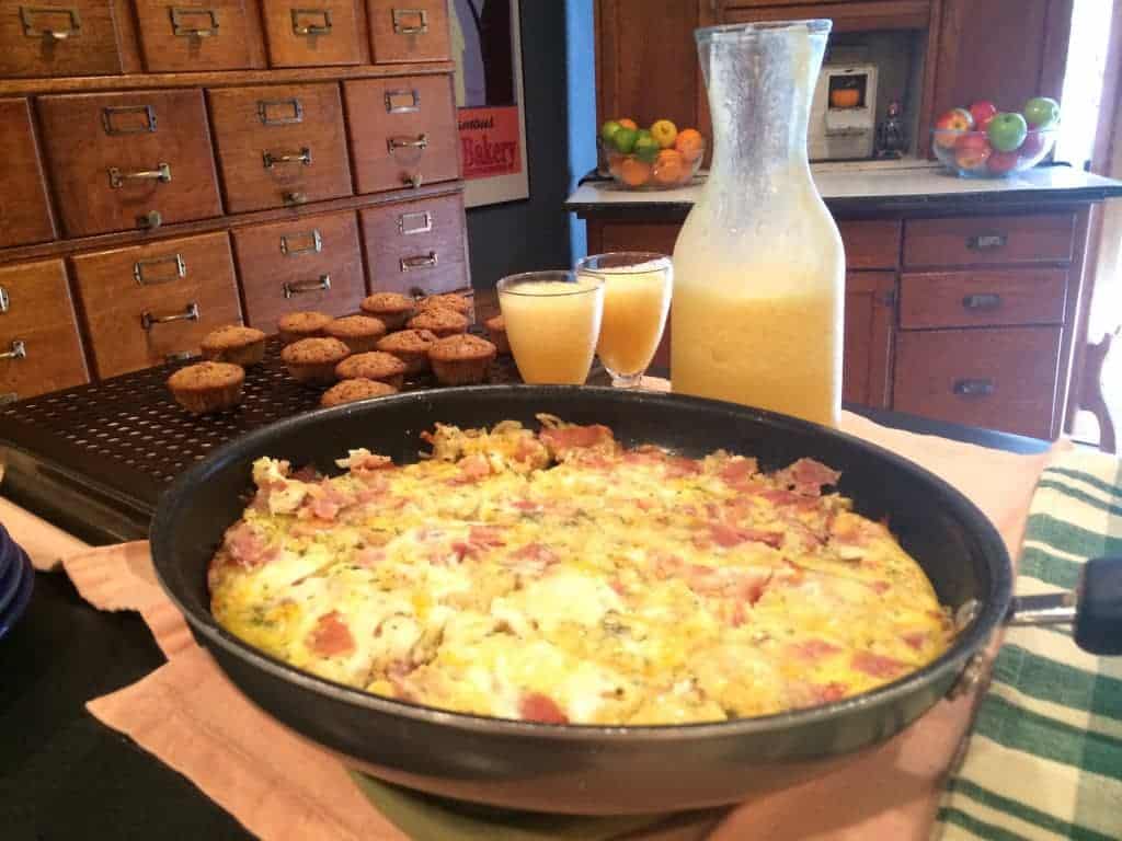 Image of the Apple Gruyere Frittata in a pan, surrounded by muffins and orange juice.