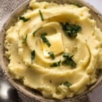 creamy mashed potatoes in a bowl topped with butter and parsley