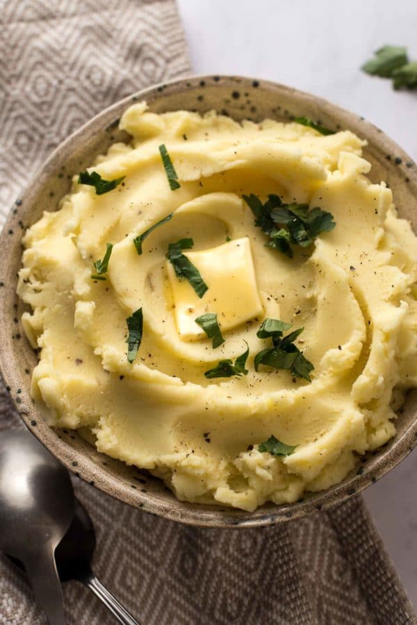 creamy mashed potatoes in a bowl topped with butter and parsley