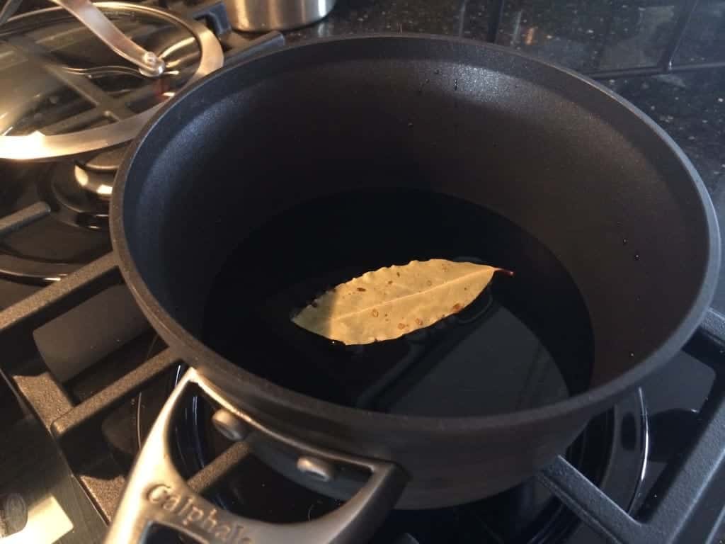 Image of vinegar and a bay leaf in a pan on a stovetop.