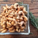 cashews in a glass bowl with rosemary sprigs.