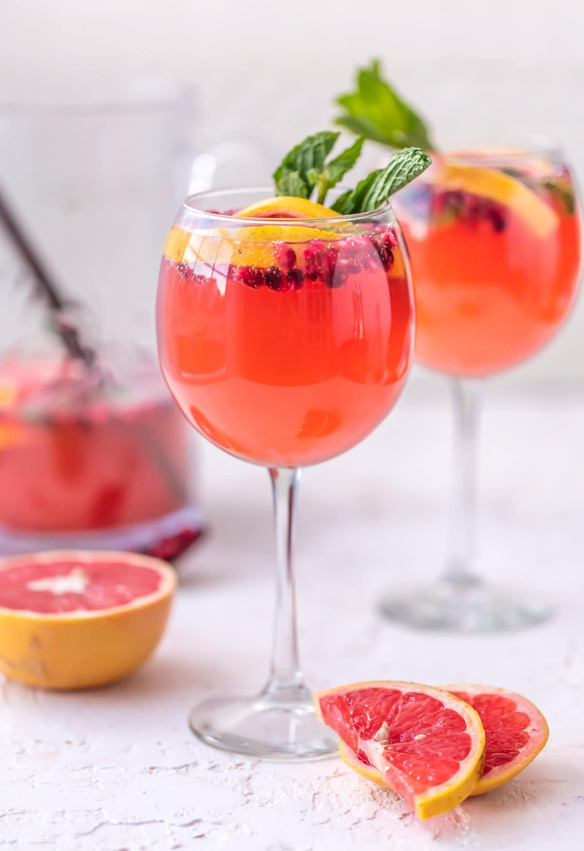 Two glasses of champagne sangria, with grapefruit, pomegranate, and mint as garnish