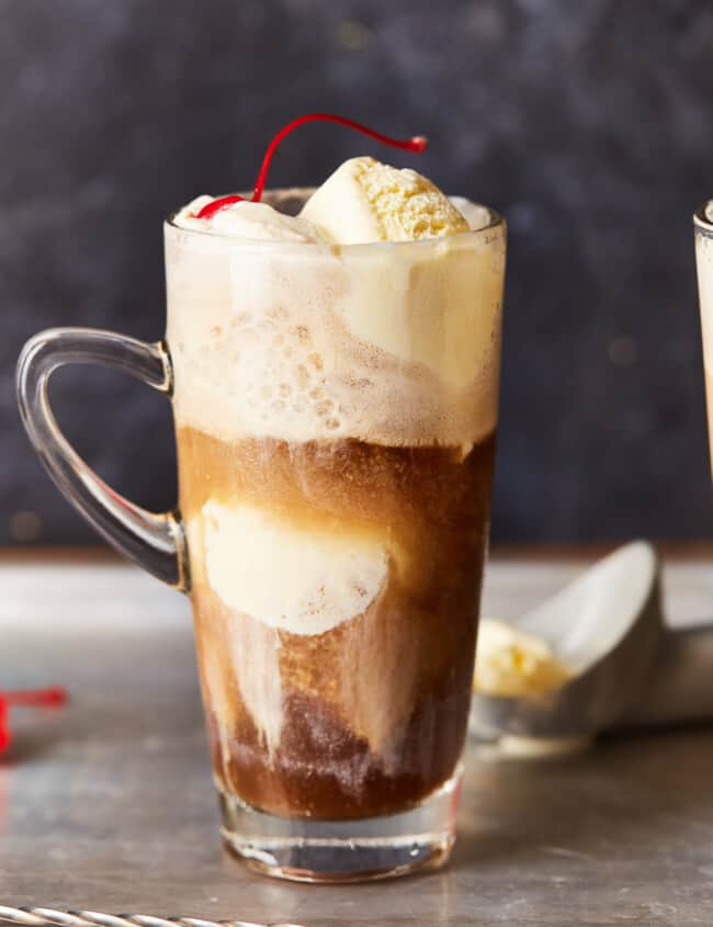 an alcoholic root beer float in a clear glass with a handle.