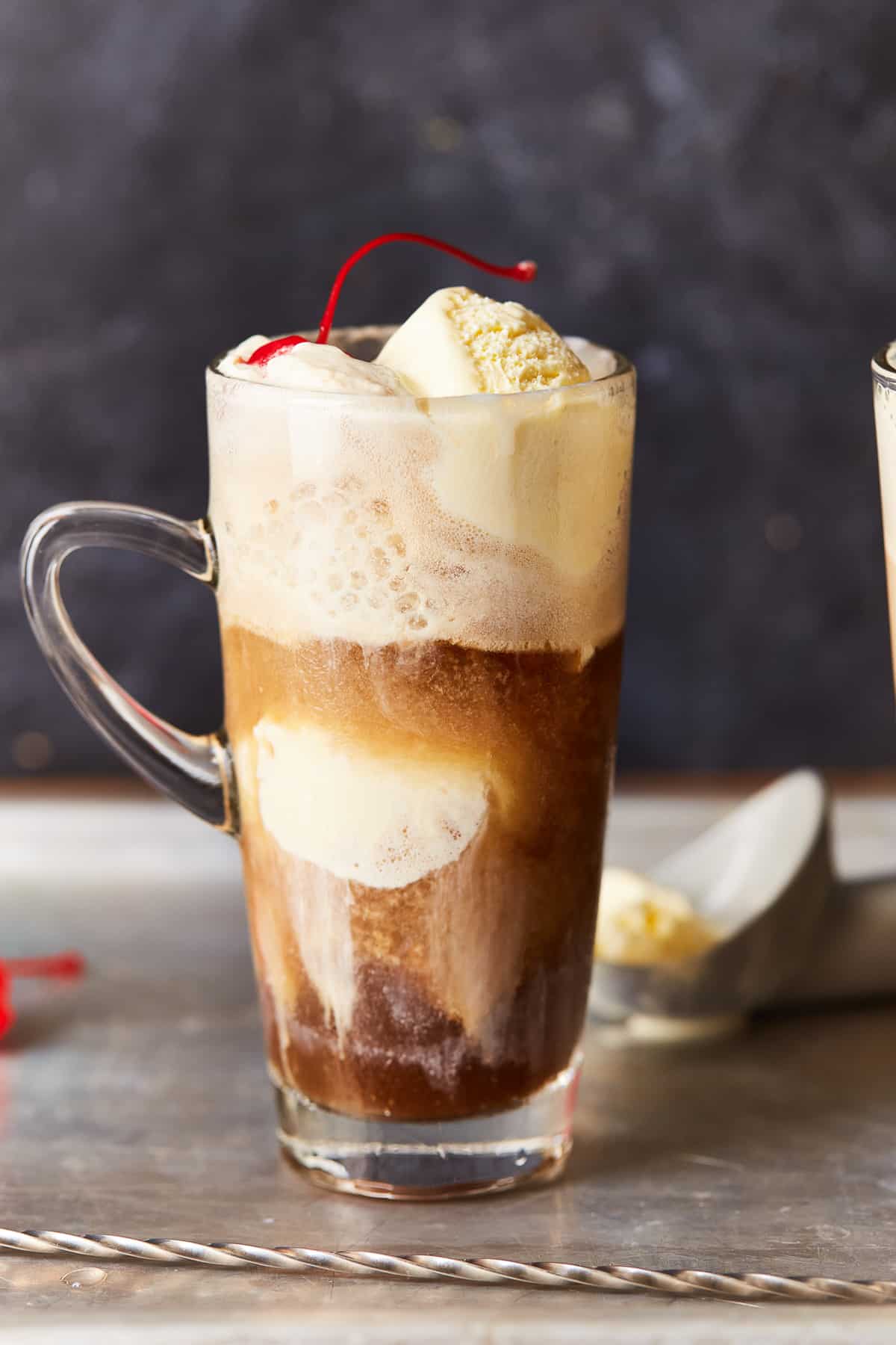 an alcoholic root beer float in a clear glass with a handle.