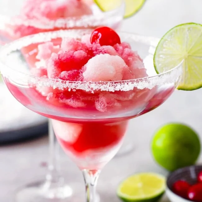 cherry limeade margarita in a margarita glass with a lime on the rim