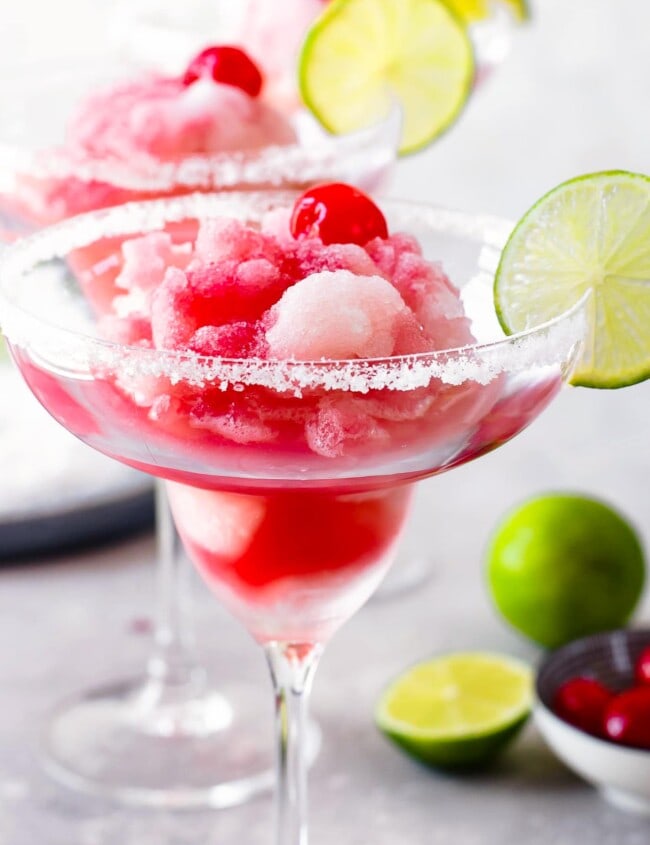 cherry limeade margarita in a margarita glass with a lime on the rim