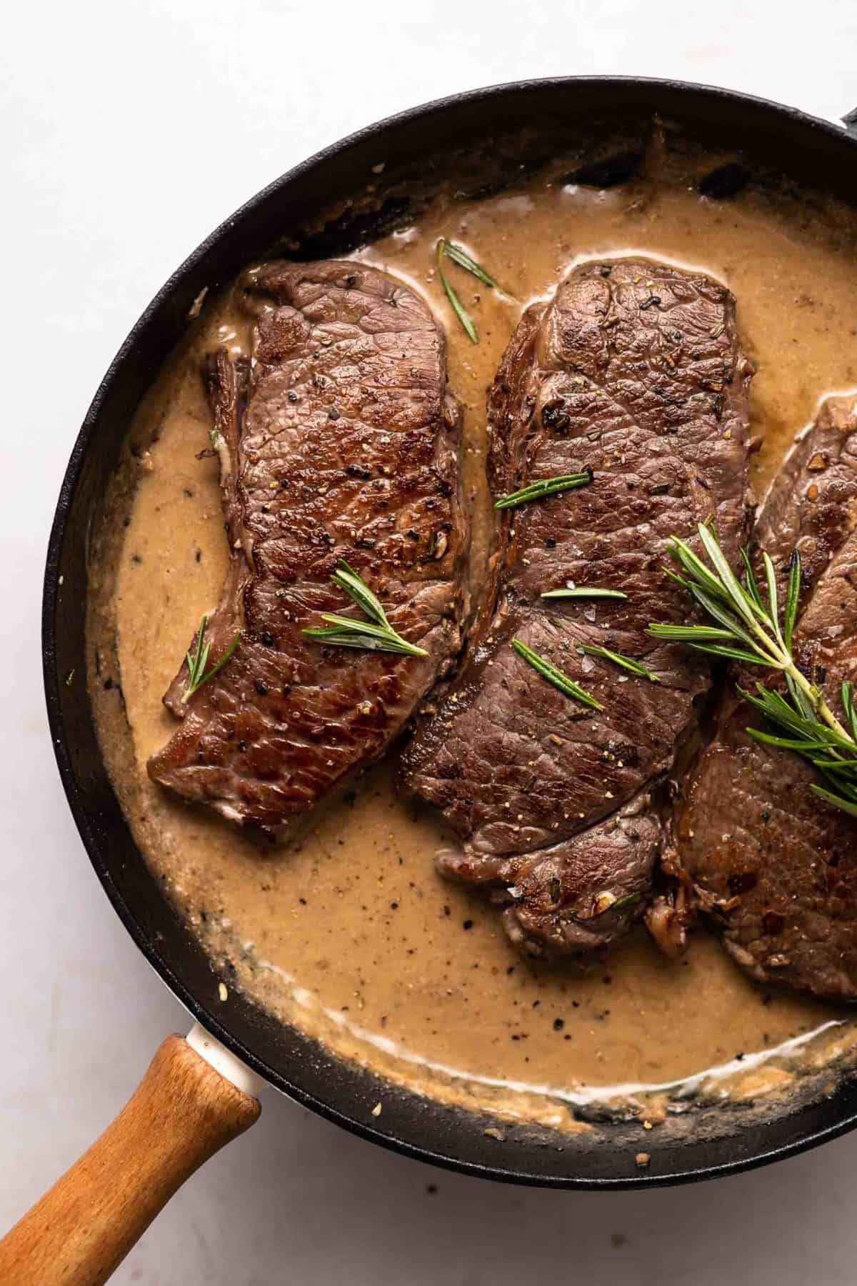 This Garlic Rosemary Steak recipe is an absolute favorite for date nights at home, romantic dinners, or just a straight up AMAZING meal. This steak with garlic, rosemary, and sherry cream sauce is so juicy, creamy, and delicious! steak in a skillet with sherry cream sauce.