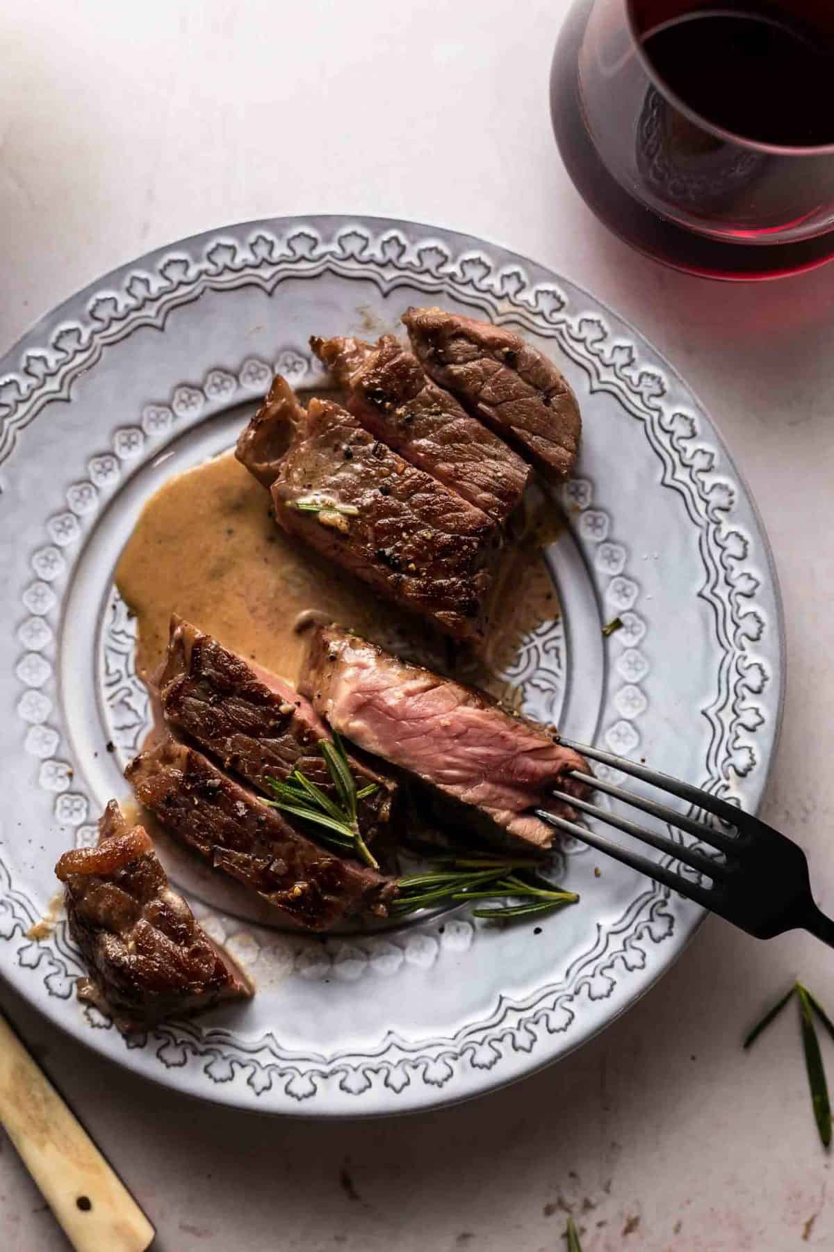 sliced strip steak on a white plate with a slice upturned to show the pink.