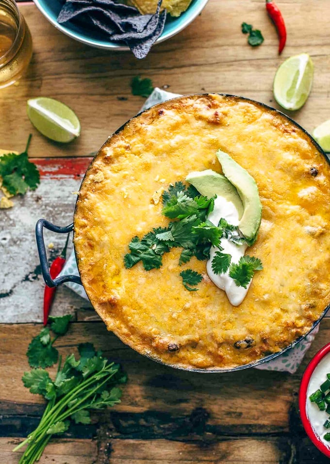 Cheesy Enchilada Dip in a large casserole dish with sour cream, avocados and cilantro.