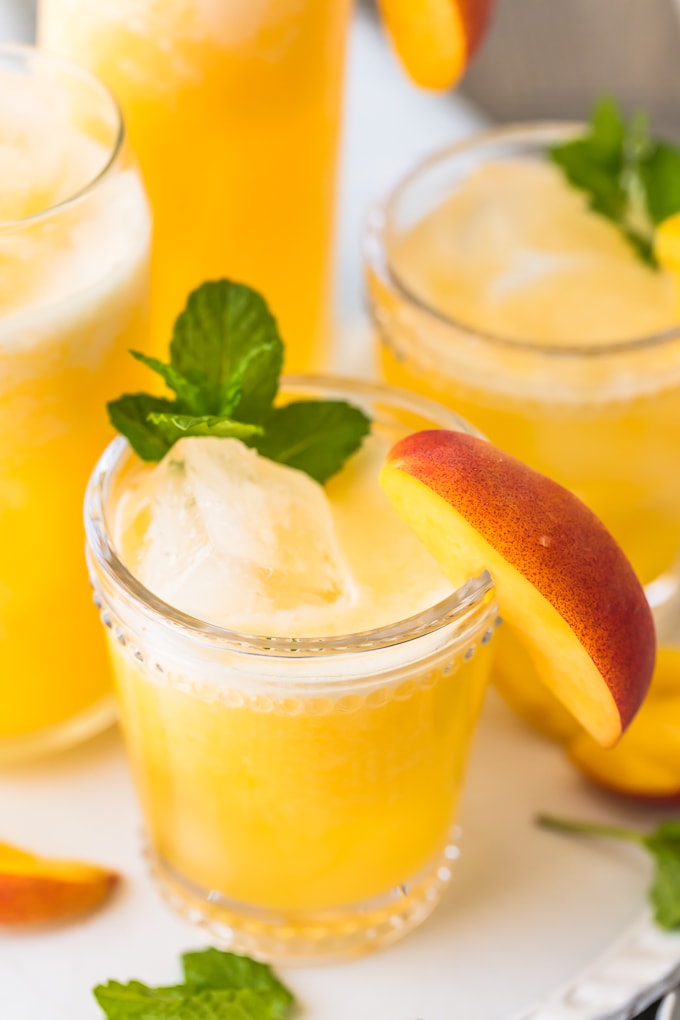 peach lemonade in a glass with ice and peach garnish on rim