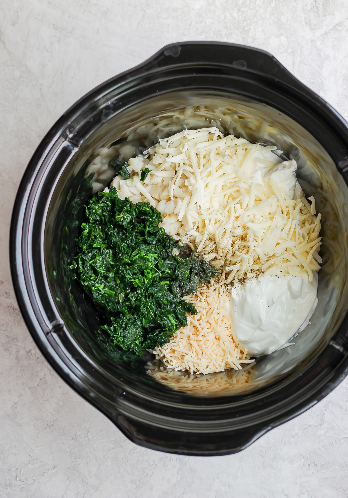 crockpot filled with spinach, cheese, and other ingredients