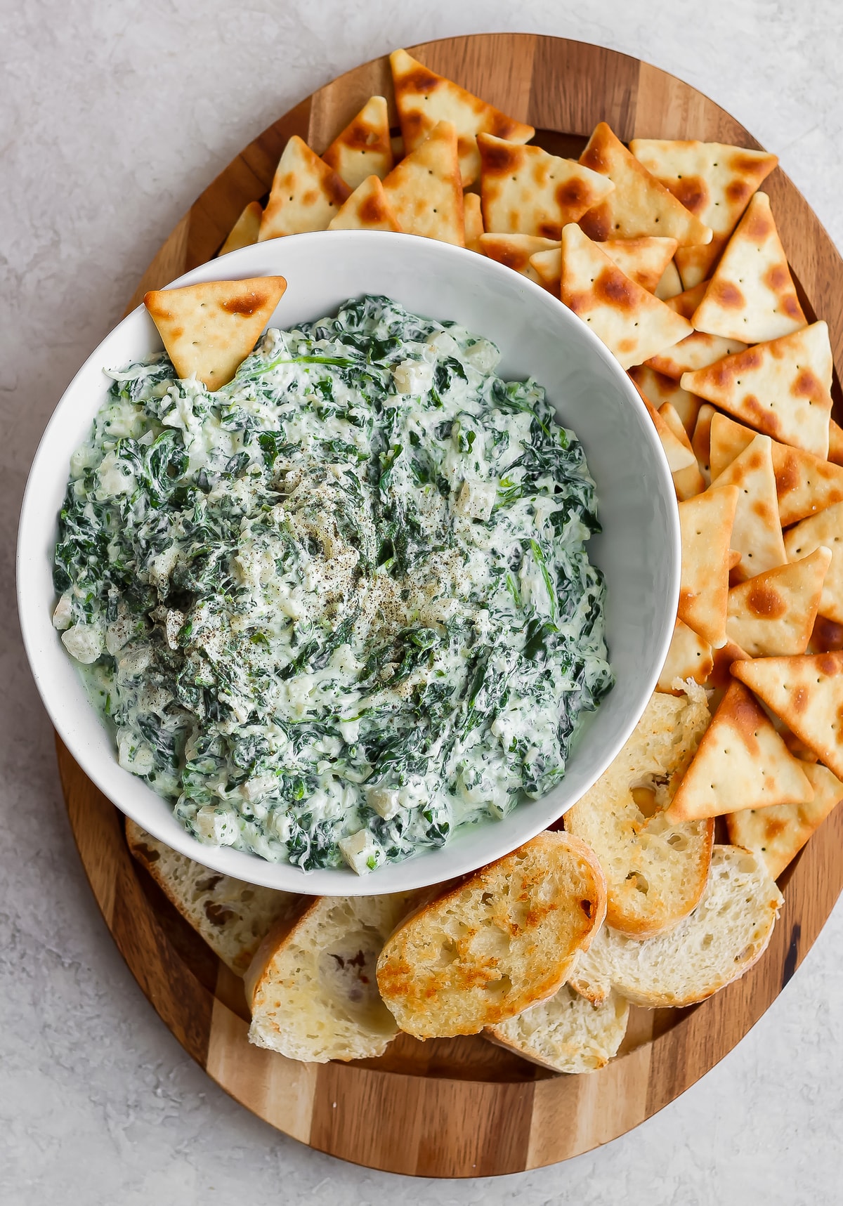 creamy spinach parmesan dip in a bowl, surrounded by a plate of crackers