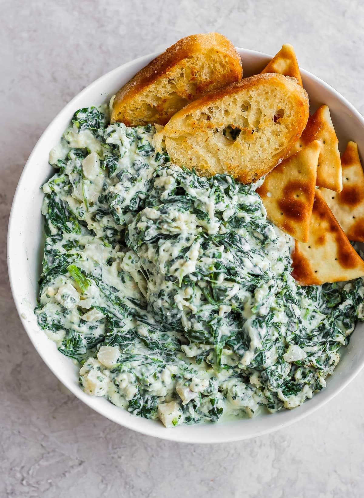 a bowl of spinach parmesan dip with crackers