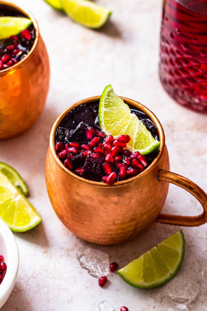 pomegranate moscow mules garnished with limes and pomegranate seeds