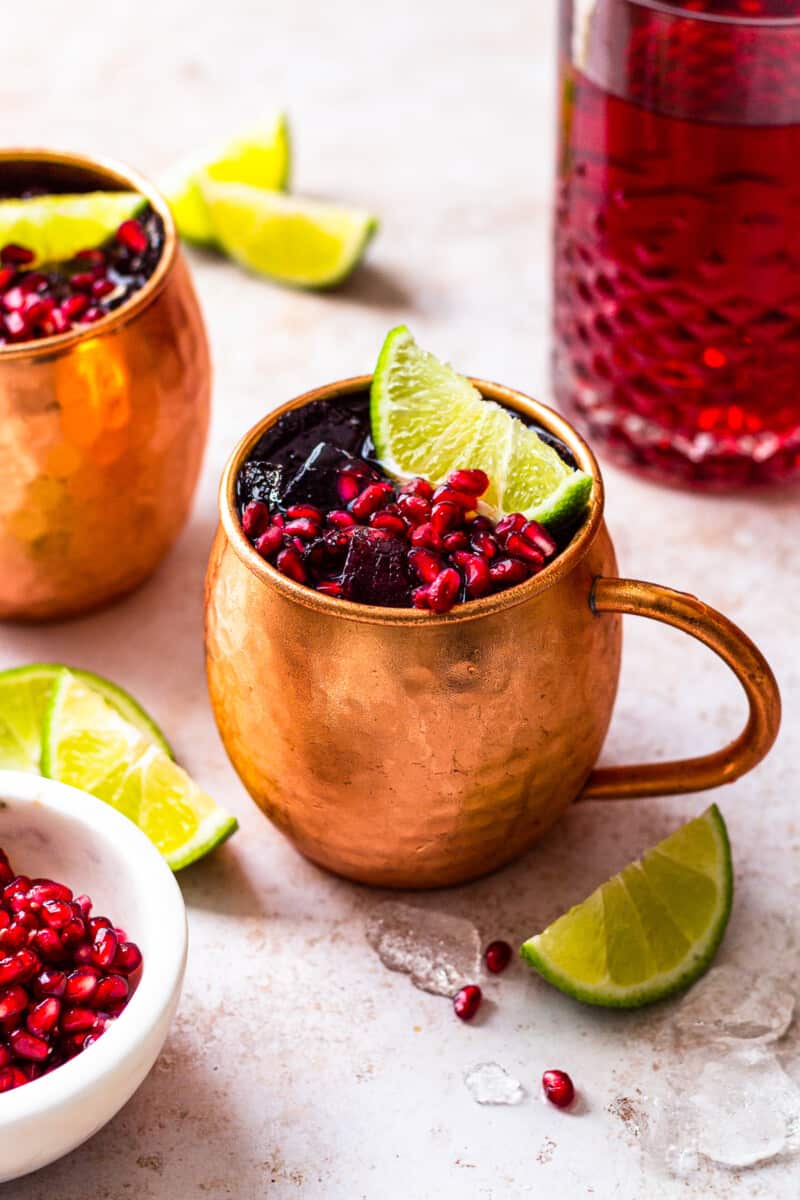 pomegranate moscow mules garnished with limes and pomegranate seeds