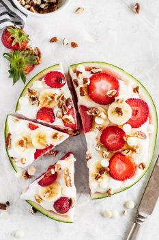 Watermelon Pizza is a delicious and fun sweet treat that everyone will enjoy! Juicy watermelon topped with a low-fat cheesecake sauce, fresh strawberries, bananas, white chocolate chips, and pecans is the ultimate (but still indulgent) healthy dessert. This refreshing cheesecake watermelon pizza is an easy summer dessert you'll be eating all season long!