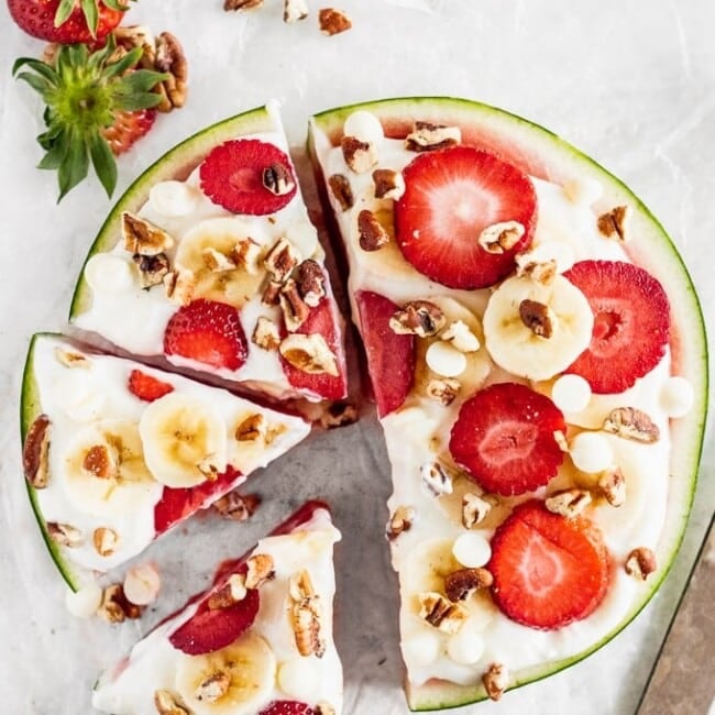 Watermelon Pizza is a delicious and fun sweet treat that everyone will enjoy! Juicy watermelon topped with a low-fat cheesecake sauce, fresh strawberries, bananas, white chocolate chips, and pecans is the ultimate (but still indulgent) healthy dessert. This refreshing cheesecake watermelon pizza is an easy summer dessert you'll be eating all season long!