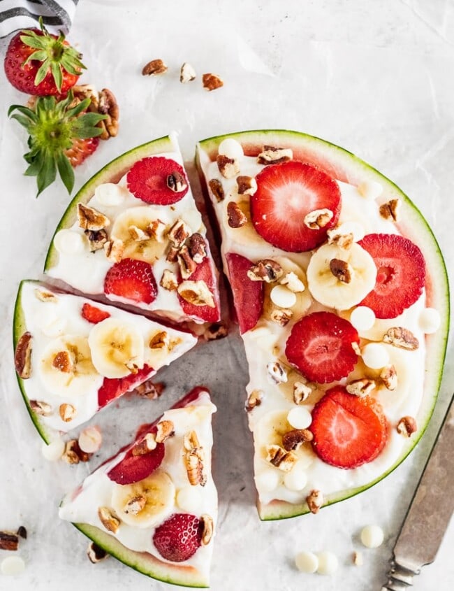 Watermelon Pizza is a delicious and fun sweet treat that everyone will enjoy! Juicy watermelon topped with a low-fat cheesecake sauce, fresh strawberries, bananas, white chocolate chips, and pecans is the ultimate (but still indulgent) healthy dessert. This refreshing cheesecake watermelon pizza is an easy summer dessert you'll be eating all season long!