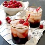 two cocktails on a tea towel with a bowl of cherries behind them