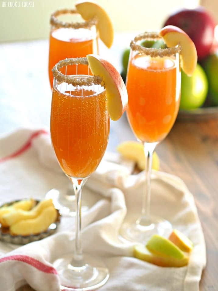 Apple Cider Mimosas - The Cookie Rookie Three flutes of Apple Cider Mimosas, garnished with apple slices.