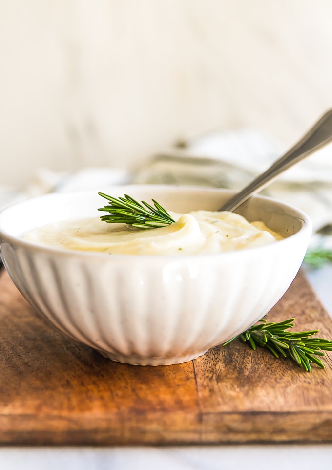 side view of a bowl of mash with a spoon and a sprig of rosemary on top.