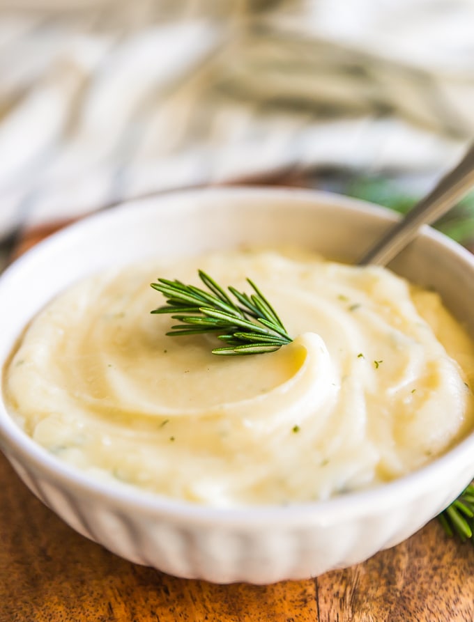 garlic mashed cauliflower in a bowl with a spoon and a sprig of rosemary.