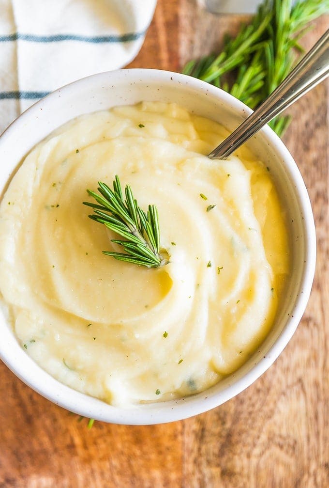 mashed cauliflower in a white bowl with a spoon and a sprig of rosemary.