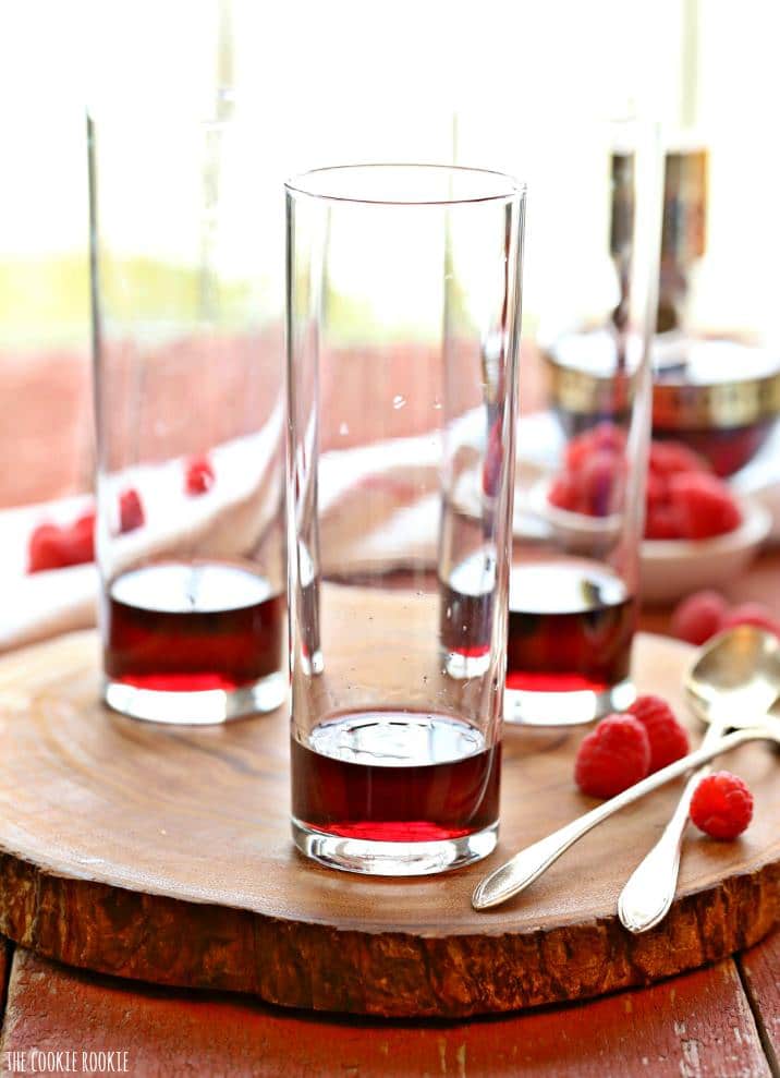 three cocktail glasses on a piece of wood filled just barely with red liquid