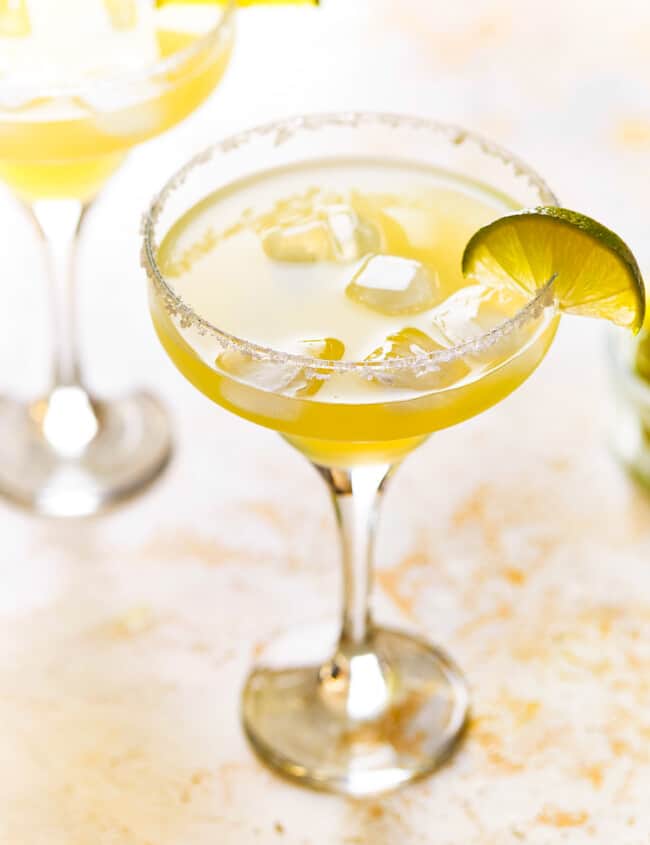 a beer margarita in a coupe glass with a salt rim and a lime wedge.