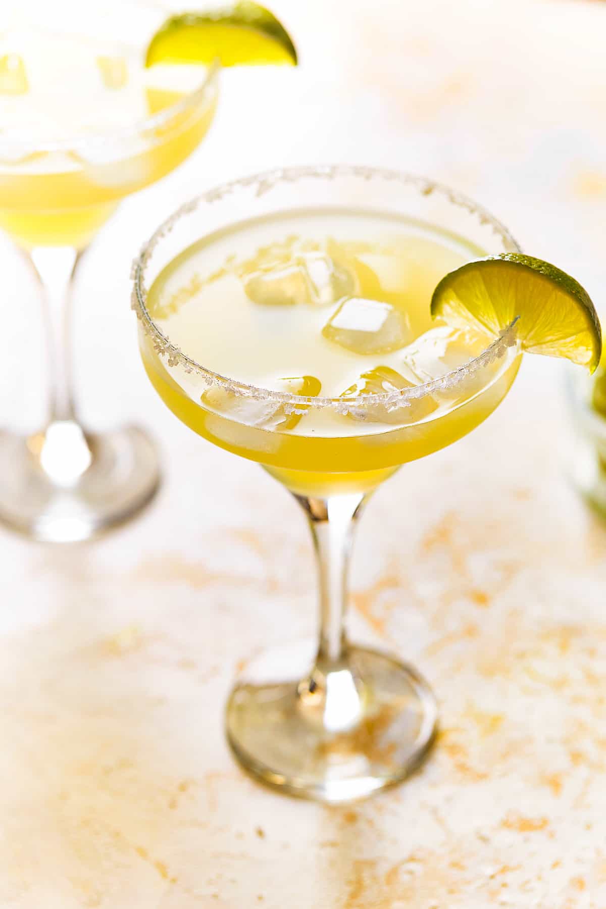 a beer margarita in a coupe glass with a salt rim and a lime wedge.