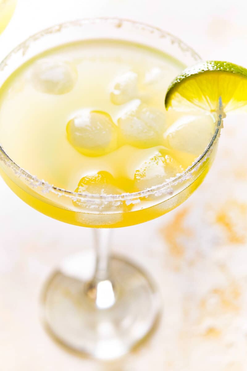 close up of a beer margarita in a coupe glass with a salt rim and a lime wedge.