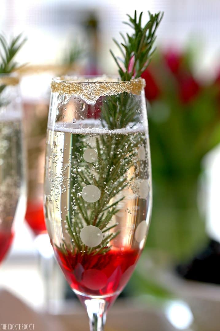 Close up view of cocktail with rosemary inside and a rimmed glass with gold sprinkles